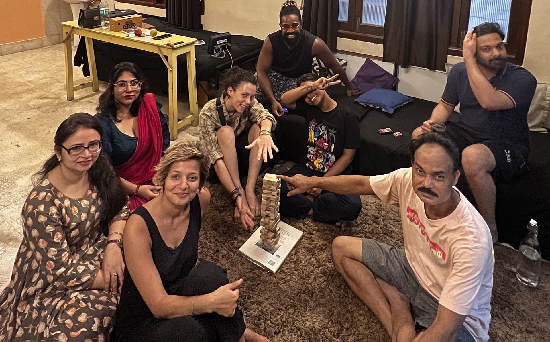 International travelers and guests smiling together around a Jenga game in the hostel lounge